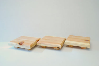 Handmade square cedar display stand with minimalist design, featuring a smooth natural wood surface and short cylindrical legs, ideal for showcasing plants, candles, or decor.